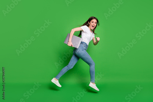 Full body profile side photo of girl jump run hold laptop wear jeans t-shirt isolated over green color background © deagreez