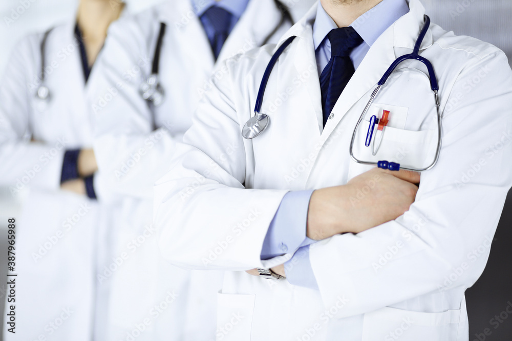 Group of modern doctors standing as a team with crossed arms and stethoscopes in hospital office. Physicians ready to examine and help patients. Medical help, insurance in health care, best desease Group of modern doctors standing as a team with crossed arms and stethoscopes in hospital office. Physicians ready to examine and help patients. Medical help, insurance in health care, best desease
