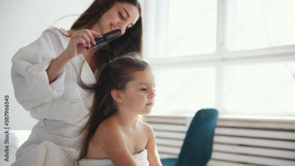 Young mother with her daughter makes hairstyle by using comb. Young mother with her daughter makes hairstyle by using comb.