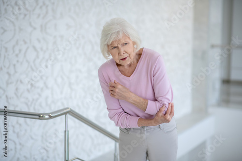 Fotografi Elderly woman in a pink shirt suffering from pain in elbow