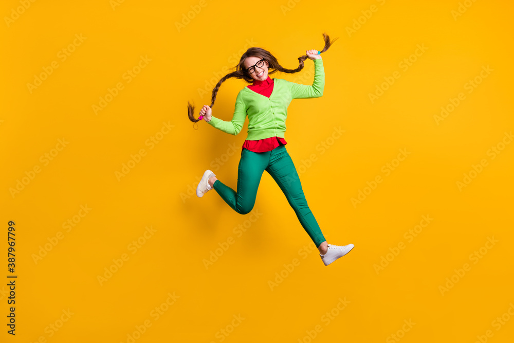 Fototapeta premium Full length body size view of attractive funky girlish cheerful girl jumping running holding pigtails isolated bright yellow color background