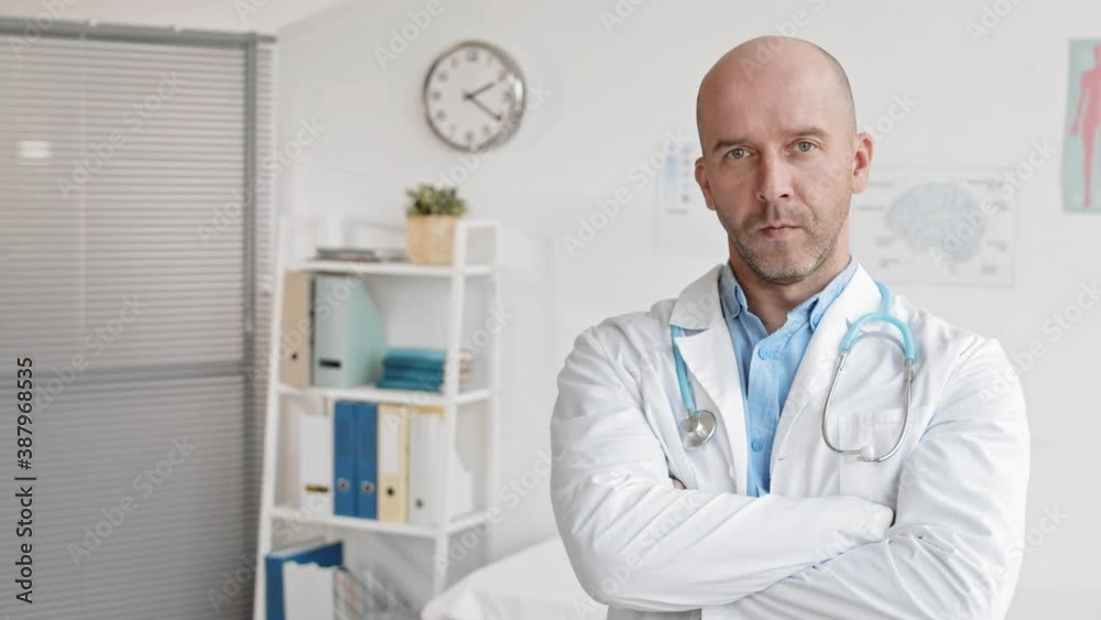 Medium close-up POV of middle-aged Caucasian male health industry worker in white gown standing in medical office, looking up on camera and crossing arms over chest Medium close-up POV of middle-aged Caucasian male health industry worker in white gown standing in medical office, looking up on camera and crossing arms over chest
