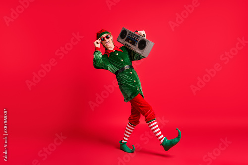 Full size profile side photo of crazy elf hold boom box go wear green costume isolated over red shine color background