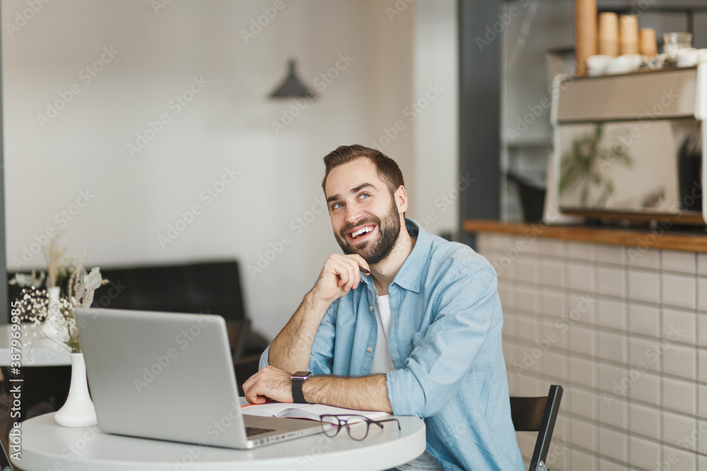 Pensive young man sitting alone at table in coffee shop cafe working studying on laptop pc computer hold pen relaxing in restaurant during free time indoors. Freelance mobile office business concept. Pensive young man sitting alone at table in coffee shop cafe working studying on laptop pc computer hold pen relaxing in restaurant during free time indoors. Freelance mobile office business concept.