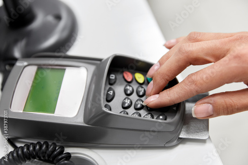 shopping, payment and finance concept - close up of hand with credit card in card-reader entering pin code