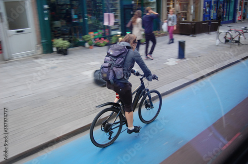 Schnelle Fahrradfahrerin auf Radweg in London mit Bewegungsunschärfe. Blauer Londoner Radweg auf der Straße neben dem Bürgersteig. © Sophia