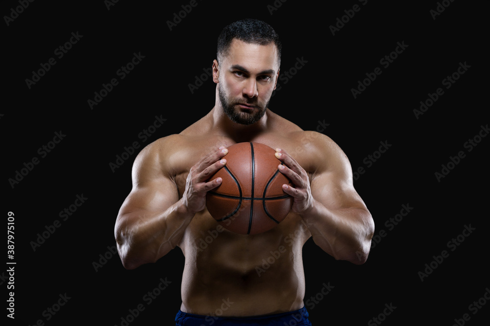 Front view portrait of an attractive sportsman holding a basketball with both hands isolated on black background