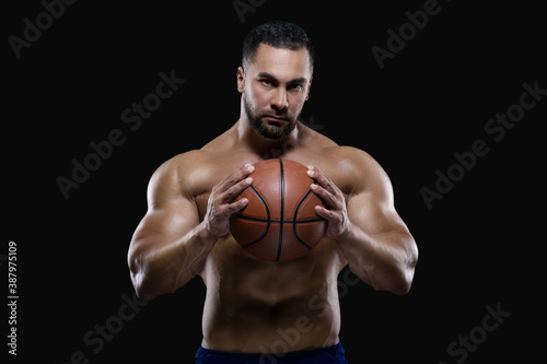 Front view portrait of an attractive sportsman holding a basketball with both hands isolated on black background