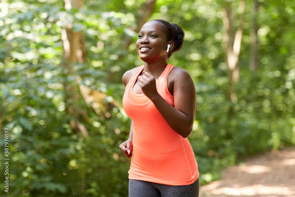 fitness, sport and healthy lifestyle concept - happy smiling young african american woman with earphones running in park fitness, sport and healthy lifestyle concept - happy smiling young african american woman with earphones running in park