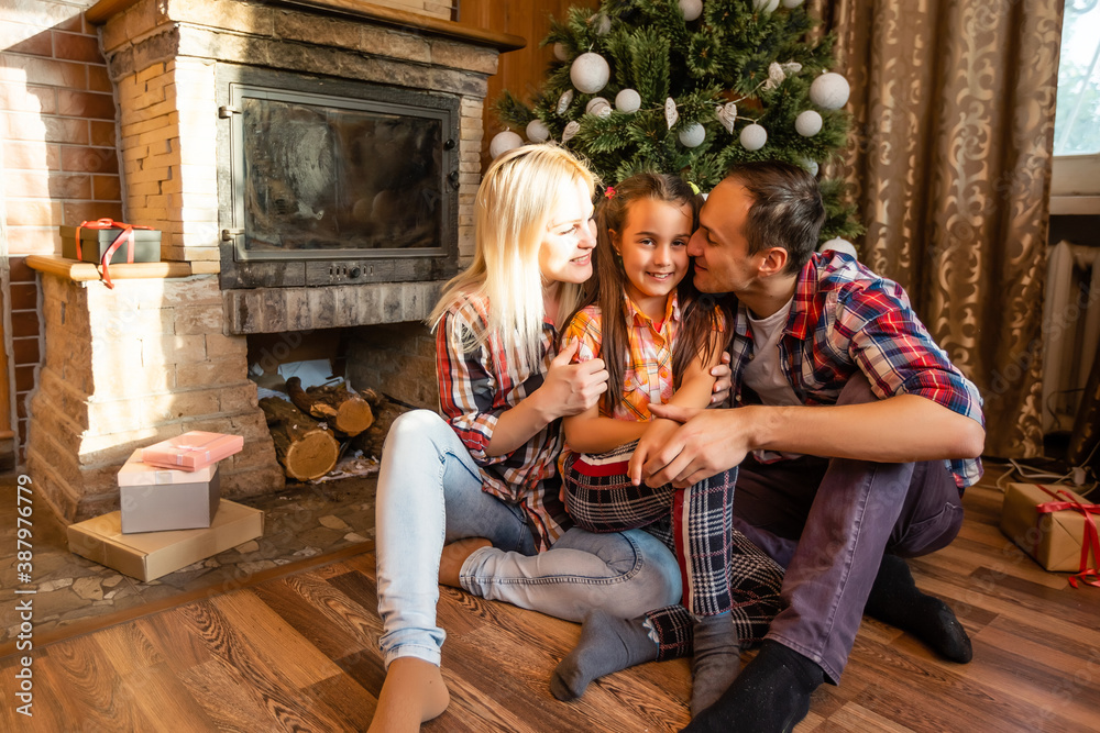 Theme Christmas and New Year family circle. Young Caucasian family sitting on wooden floor home in living room near fireplace Christmas tree.