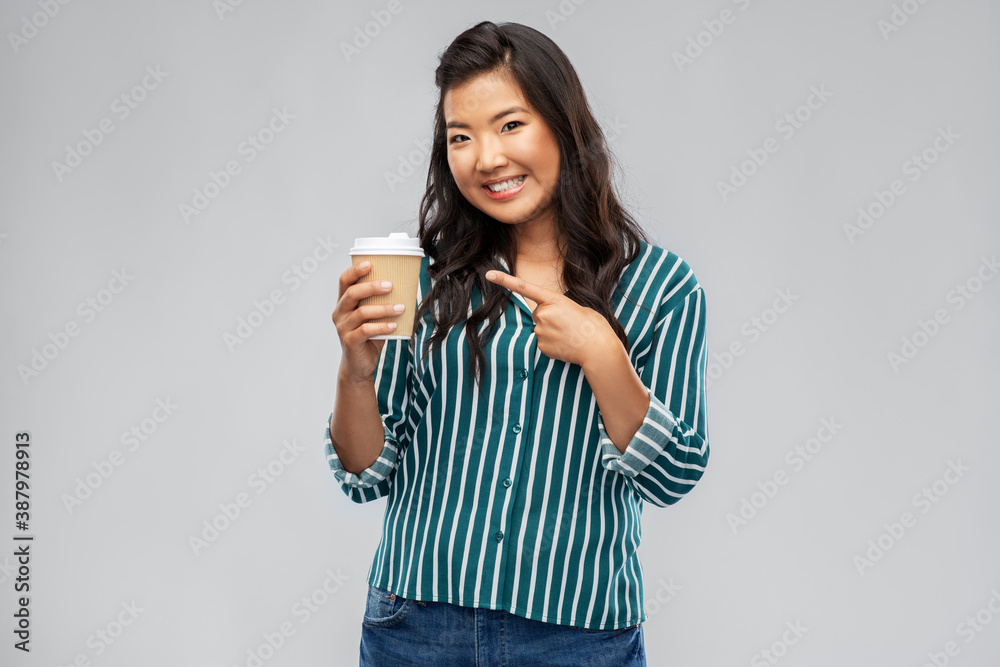 people and drinks concept - happy young asian woman showing takeaway coffee paper cup over grey background people and drinks concept - happy young asian woman showing takeaway coffee paper cup over grey background