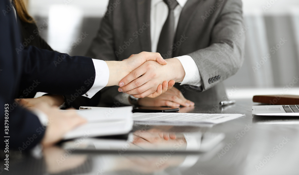 Unknown businessman shaking hands with his colleague or partner above the glass desk in modern office, close-up. Business people group at meeting Unknown businessman shaking hands with his colleague or partner above the glass desk in modern office, close-up. Business people group at meeting