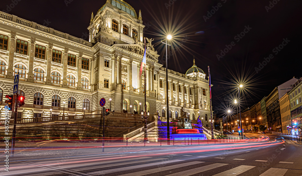 A czech National Museum in Prague in night with illuminated front fasade and colourful fountain. Light trails of cars in the foreground.