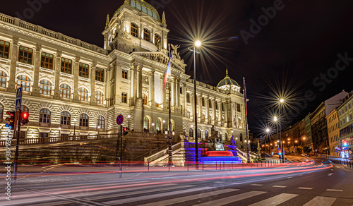 A czech National Museum in Prague in night with illuminated front fasade and colourful fountain. Light trails of cars in the foreground.