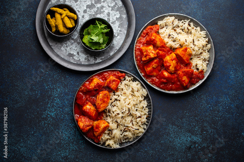 Chicken tikka masala dish with rice, flat Indian bread and spices in rustic metal plates on concrete background top view. Chicken tomato curry, turmeric root, fresh cilantro, traditional Indian meal