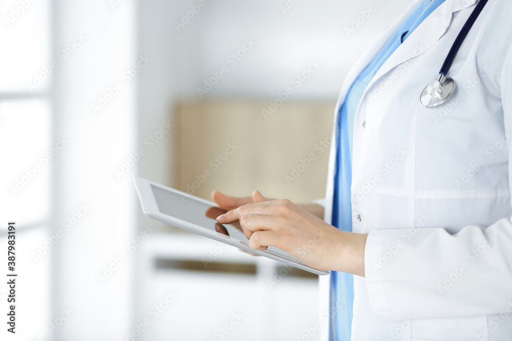Unknown woman-doctor standing in clinic and using tablet pc, close-up. Data in medicine and healthcare Unknown woman-doctor standing in clinic and using tablet pc, close-up. Data in medicine and healthcare