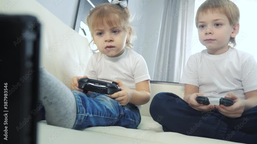 children play console in lifestyle gamepads teamwork. kids a boy and a girl are playing a portable set-top box in a TV controller. happy family little boy and girl have fun online games children play console in lifestyle gamepads teamwork. kids a boy and a girl are playing a portable set-top box in a TV controller. happy family little boy and girl have fun online games
