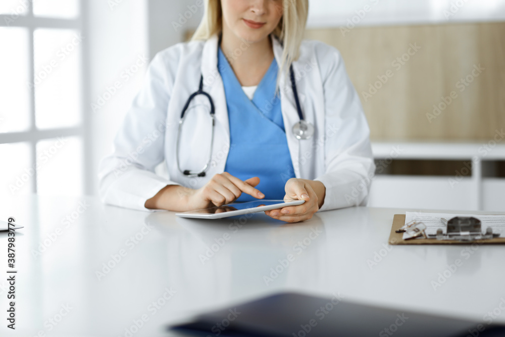 Unknown woman-doctor standing in clinic and using tablet pc, close-up. Data and best service in medicine and healthcare