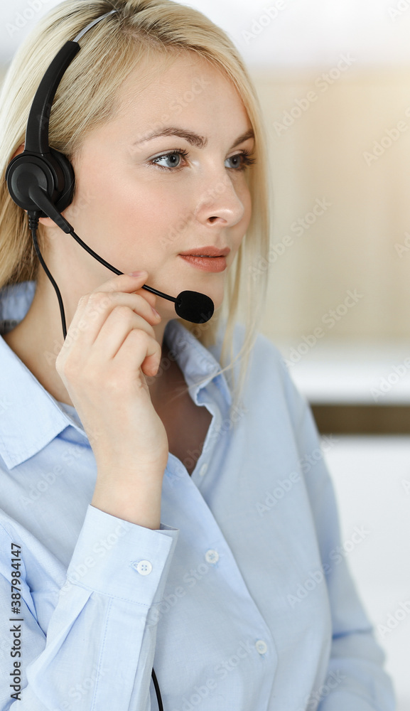 Blonde business woman sitting and communicated by headset in sunny call center office Blonde business woman sitting and communicated by headset in sunny call center office