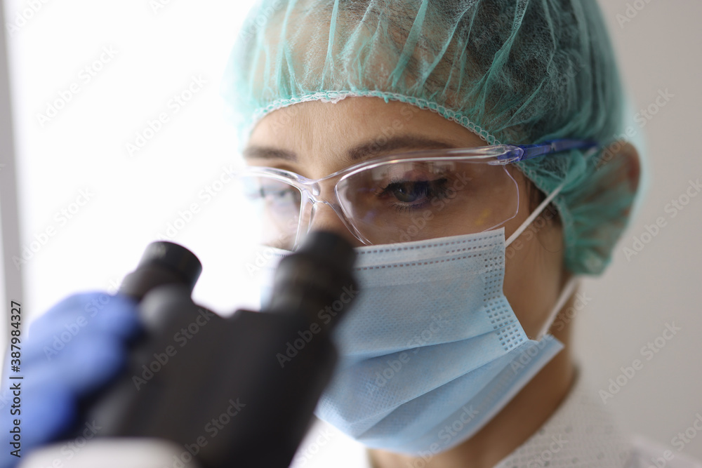 Researcher wearing mask and glasses looks through microscope. Development of new drugs and vaccines concept