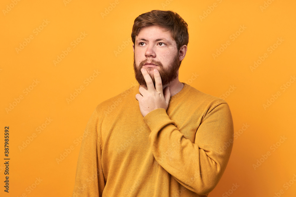 Image of a man in basic clothing, thinking and touching his chin, looking to the side, isolated on a yellow background. The bearded man makes a decision. to be or not to be Image of a man in basic clothing, thinking and touching his chin, looking to the side, isolated on a yellow background. The bearded man makes a decision. to be or not to be
