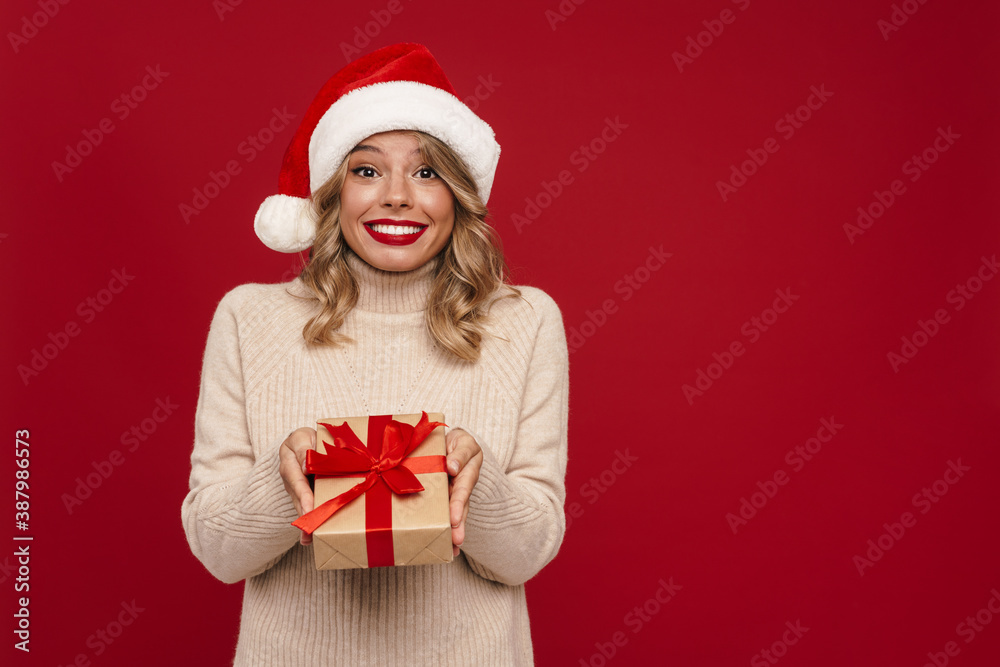 Beautiful happy girl in Santa Claus hat showing gift box Beautiful happy girl in Santa Claus hat showing gift box