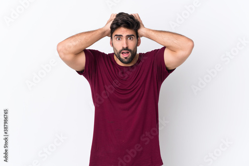 Young handsome man with beard over isolated white background frustrated and takes hands on head