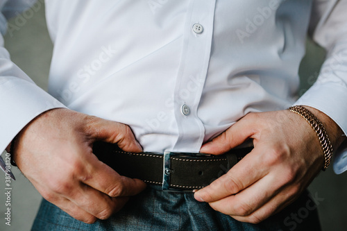 A man in pants and shirt buttoned a leather trouser belt. Groom Dress up a belt with buckle. Businessman wear leather stylish belt. New classic belt.