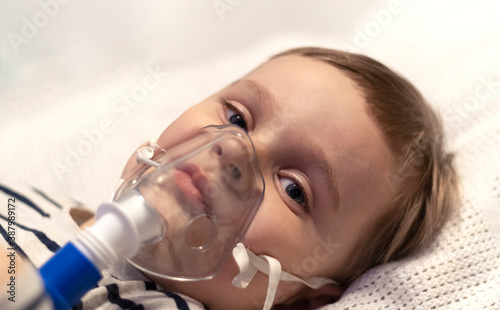 The child makes inhalation with a nebulizer in the house. Nebulizer medical device for inhalation treatment with mask on child.