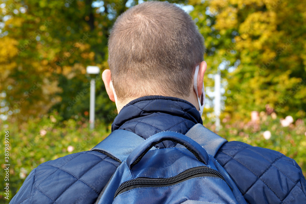 a man in a blue jacket and a blue backpack stands with his back against the background of trees with yellow and green leaves on an autumn day a man in a blue jacket and a blue backpack stands with his back against the background of trees with yellow and green leaves on an autumn day