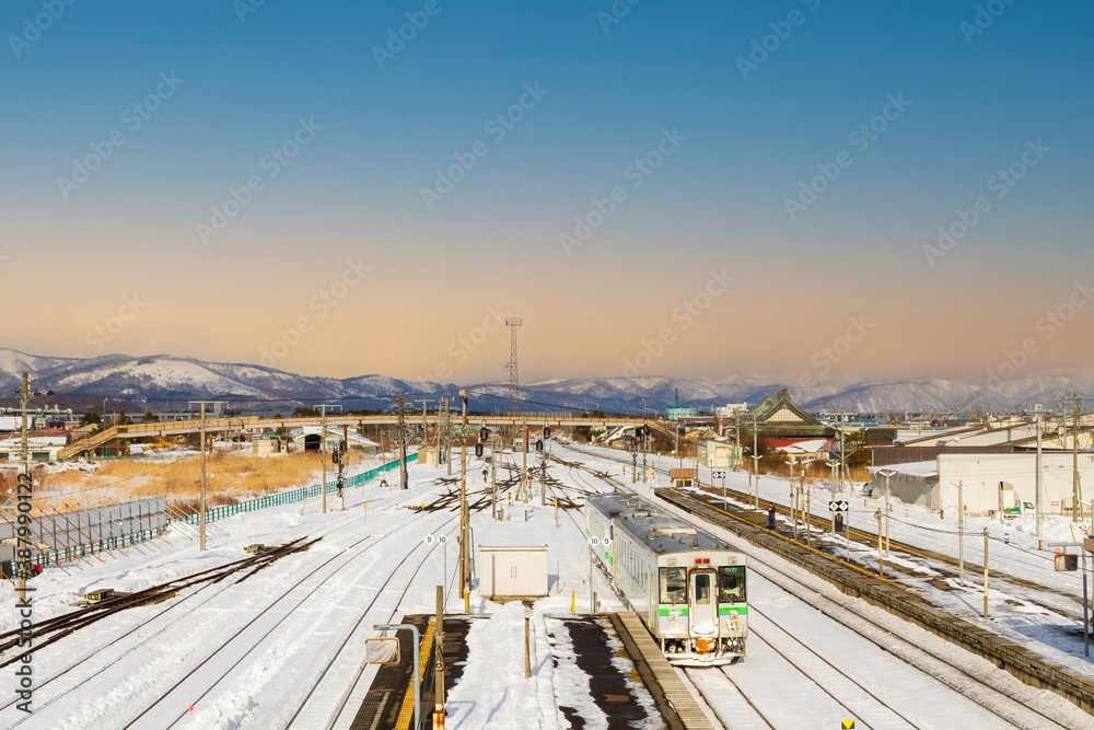 Landscape view of railway junction at train station that covered by snow in winter with mountain in the background at the evening which sky is orange and blue while sunset.