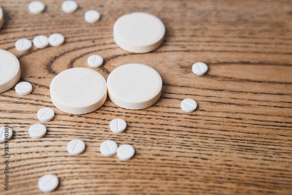 white small and large round pills on a wooden background close-up. Pharmaceutical drugs for the treatment of diseases on a wooden table white small and large round pills on a wooden background close-up. Pharmaceutical drugs for the treatment of diseases on a wooden table