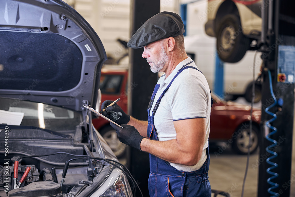 Bearded male worker writing on clipboard at auto repair station Bearded male worker writing on clipboard at auto repair station
