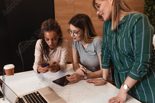 Group of young women in casual wear discussing architectural designs in the creative office.