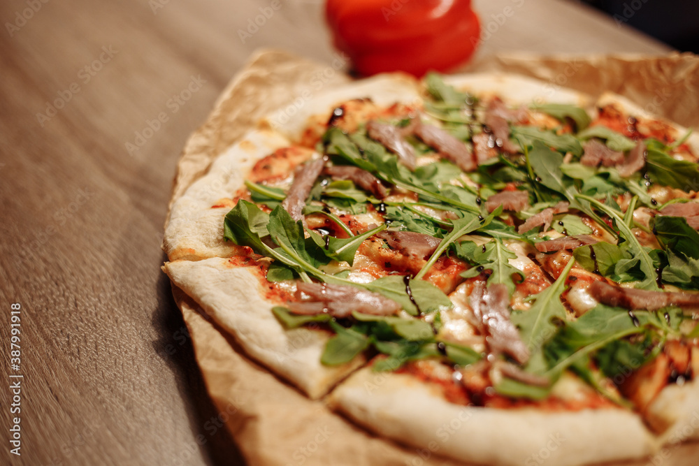 fresh pizza with herbs, tuna and balsamic sauce on food paper on a wooden table in a cozy cafe, bell pepper in the background fresh pizza with herbs, tuna and balsamic sauce on food paper on a wooden table in a cozy cafe, bell pepper in the background