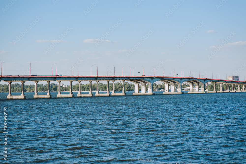 A large concrete old bridge stands in a blue river, the sea against the background of the city and the sky.