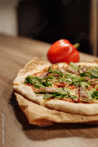 fresh pizza with herbs, tuna and balsamic sauce on food paper on a wooden table in a cozy cafe, bell pepper in the background