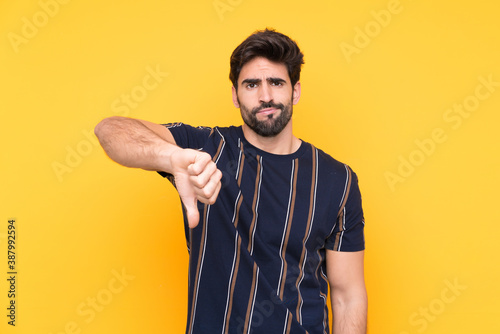 Young handsome man with beard over isolated yellow background showing thumb down sign © luismolinero