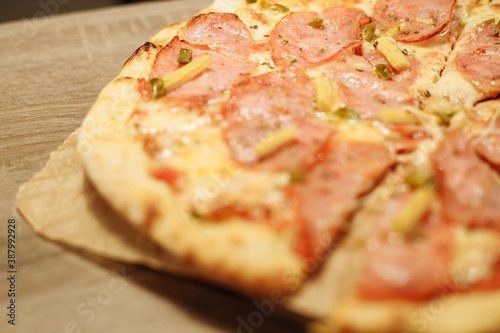 pizza with sausage, mini corn, jalapeno pepper on food paper on a wooden table in warm light