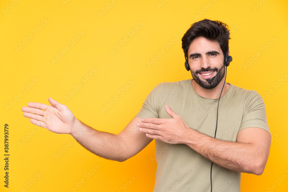 Telemarketer man working with a headset over isolated yellow background extending hands to the side for inviting to come Telemarketer man working with a headset over isolated yellow background extending hands to the side for inviting to come