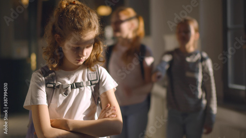 Outcast sad girl at school with group of friends laughing behind photo