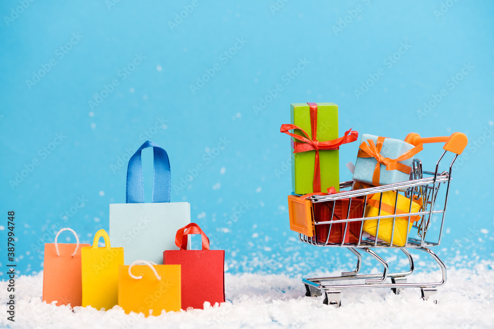 Tiny paper bags near trolley with bunch of little gifts on blue background, new year concept - obrazy, fototapety, plakaty 