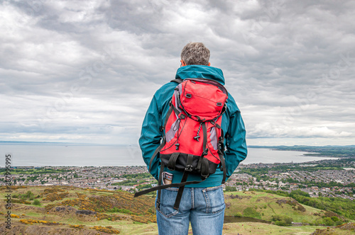 Man with bagpack looking at the Edinburgh cityscape on a cloudy day. Concept: travel to Scotland, Scottish landscapes