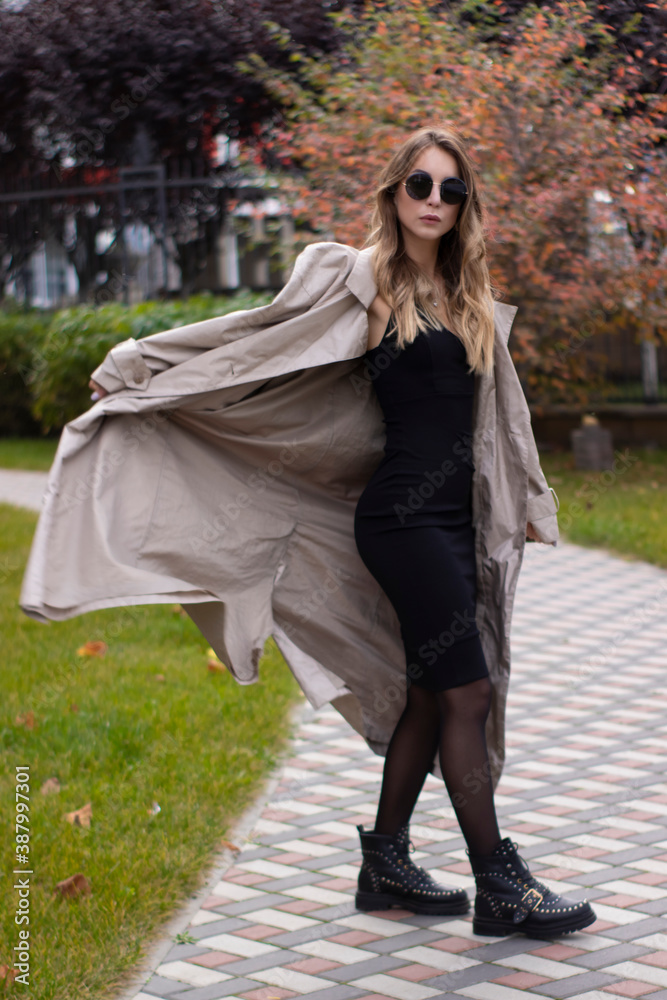 attractive slim young brunette in fashionable trench, black dress and sunglasses in park. autumn, yellow leaves. attractive slim young brunette in fashionable trench, black dress and sunglasses in park. autumn, yellow leaves.