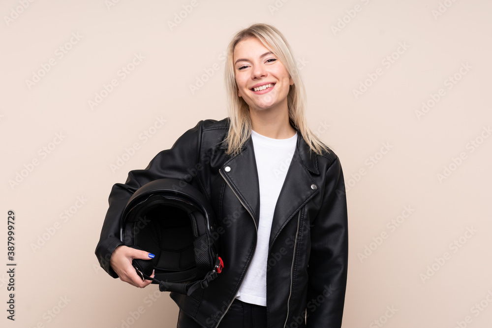 Young blonde woman with a motorcycle helmet over isolated background smiling a lot Young blonde woman with a motorcycle helmet over isolated background smiling a lot
