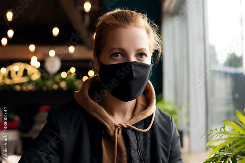 Young woman in protective mask sits in a cafe