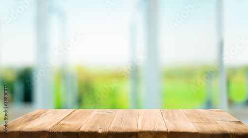 The top of the wooden table on the blur of the windowpane. Green color from a vegetable garden on the morning background. For product montage display.