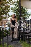 beautiful slim young brunette in fashionable trench coat and black dress walking near stairs. autumn, yellow leaves. .