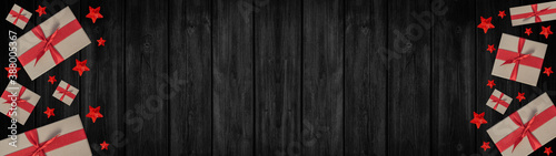 Festive Christmas / Advent background banner panorama - Top view / above view from gift boxes with red ribbon and stars, on rustic black wooden boards, wood table texture
