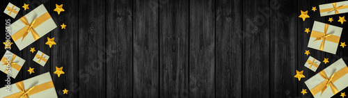 Festive Christmas / Advent background banner panorama - Top view / above view from yellow golden gift boxes with ribbon and stars, on rustic black wooden boards, wood table texture